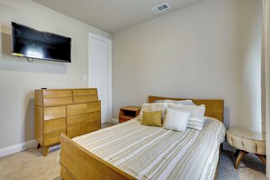 Un dormitorio con cama, cómoda de madera, televisor montado en la pared y una mesita de noche.