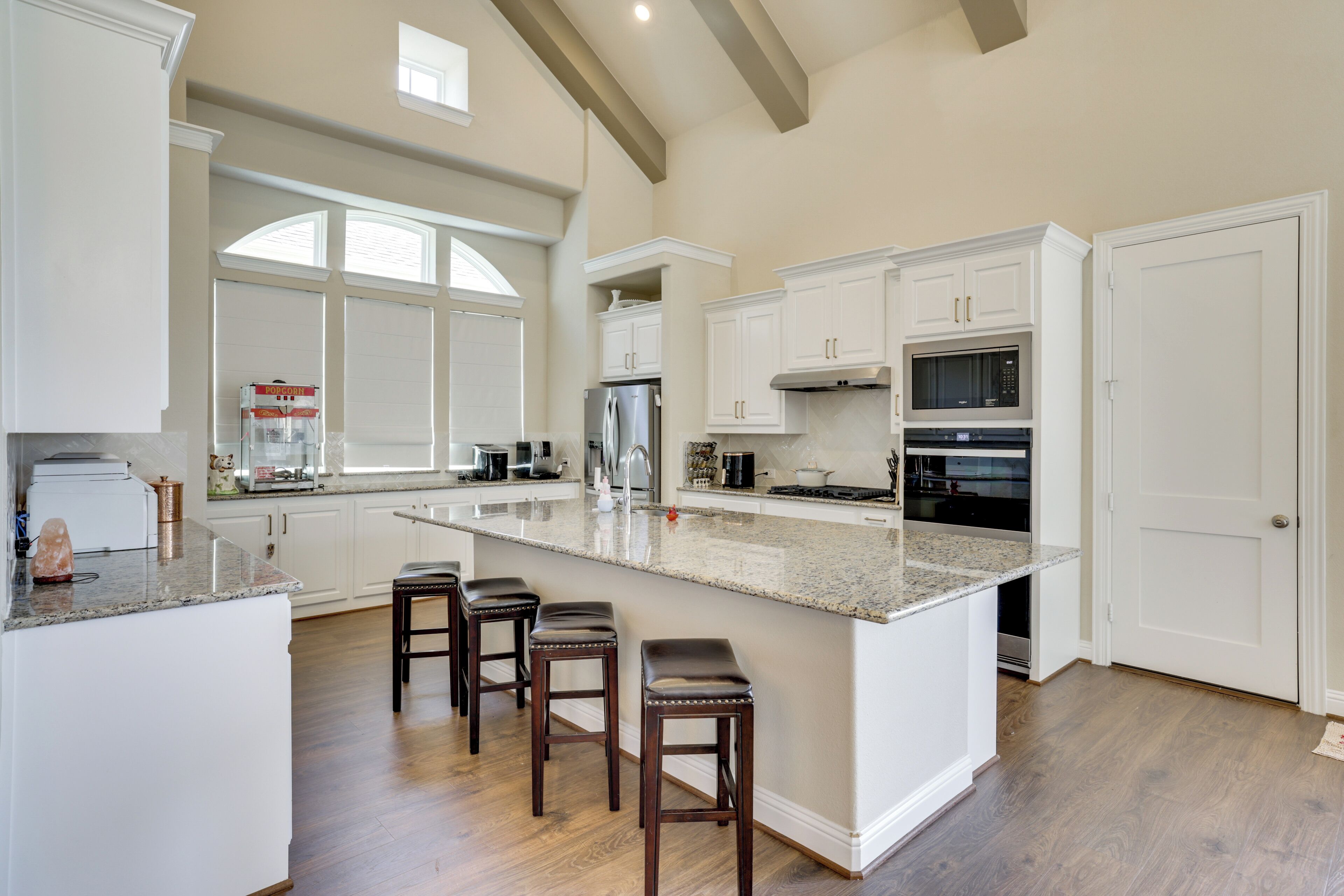 A spacious kitchen with a large island, white cabinetry, and a stone countertop.