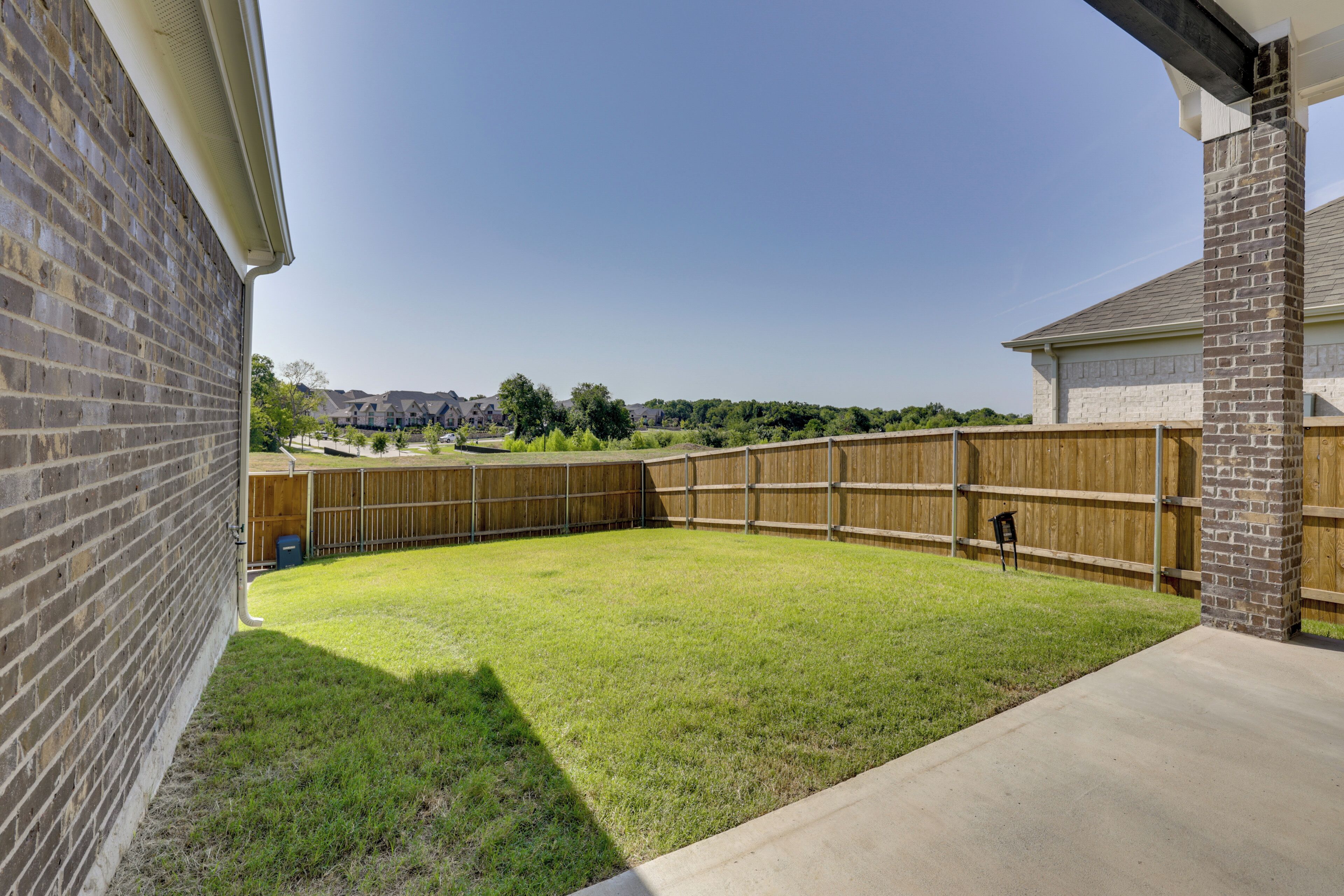 A backyard with a wooden fence, a grassy lawn, and a brick wall.