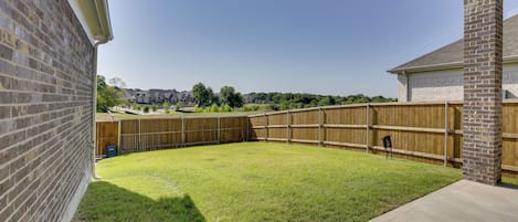 A backyard with a wooden fence, a grassy lawn, and a brick wall.