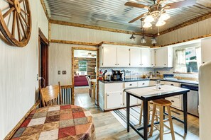A kitchen with wooden cabinets, a central island with stools, a ceiling fan, and a window with curtains.