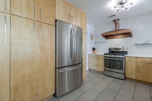 Een moderne keuken met roestvrijstalen apparatuur, houten kastjes en een witte betegelde achterwand.