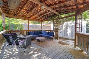 Een overdekt terras met houten vloer, een bank en een barbecue.