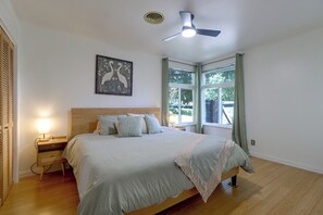 Ein Schlafzimmer mit Bett, Nachttischlampen, Deckenventilator, einem Fenster mit Vorhängen und einem Wandbild.