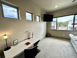A modern room with a white desk, black chair, and a sofa. There are multiple windows and a flat-screen TV mounted on the wall. - 3 King Beds | 3 Baths | 2-Car Garage (Poncha Springs)