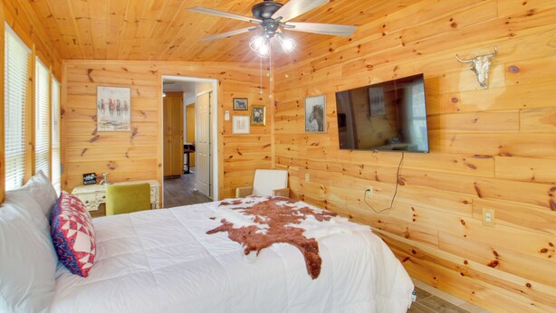 Ein Zimmer mit Holzwänden, einem Bett, einem Deckenventilator und einem an der Wand befestigten Fernseher.
