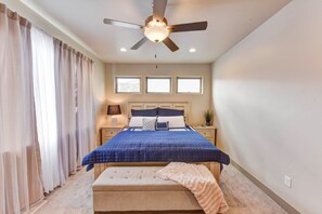Une chambre à coucher avec un lit, un ventilateur de plafond, une table de chevet, une lampe et une fenêtre.