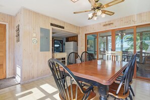 Un coin repas avec une table et des chaises en bois, un ventilateur de plafond et une vue à travers des portes vitrées.