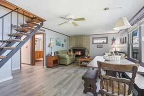 A spacious living area with a wooden staircase, a fireplace, and a dining table with chairs. - Lakefront Paradise on Lake Wallenpaupack w/ Dock (Hawley)