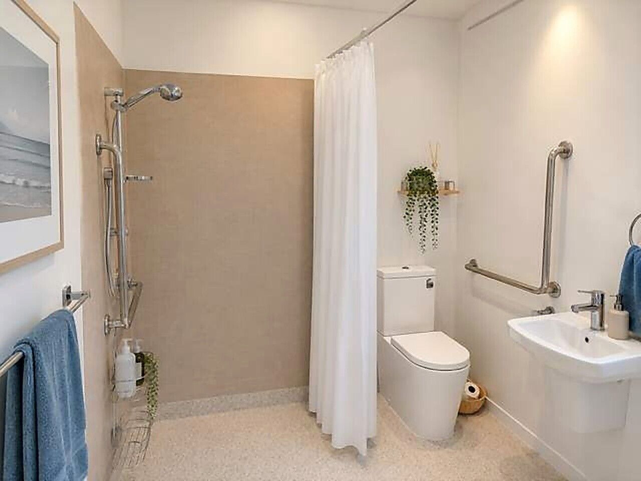 A bathroom with a shower, toilet, and sink, equipped with grab bars and a white curtain.
