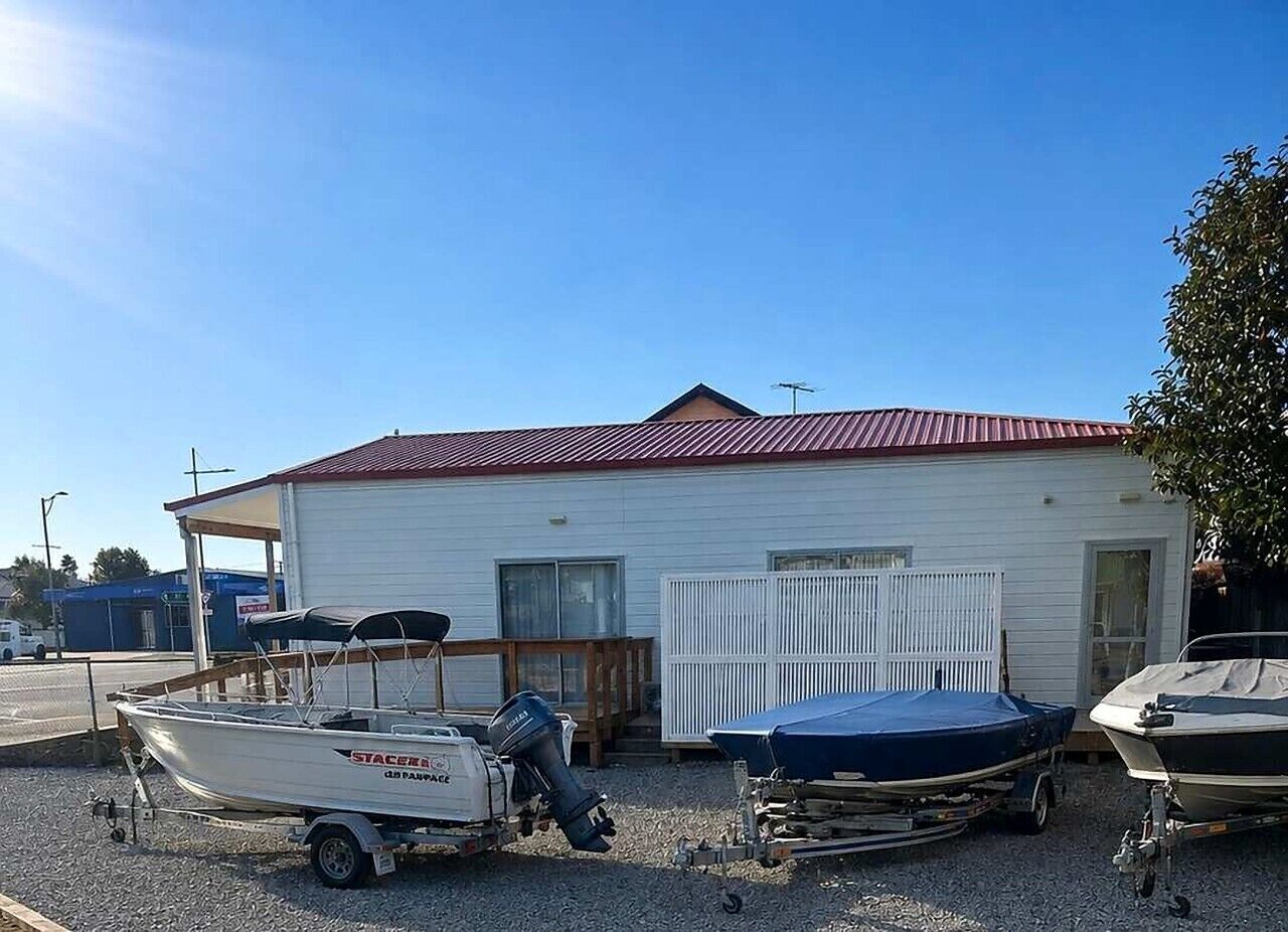 Un pequeño edificio con techo rojo, una zona de amarre cubierta y dos barcos sobre remolques.