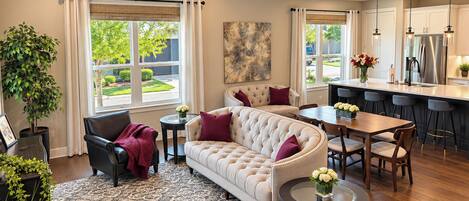 A modern living room with a sofa, chairs, a coffee table, and a dining area with a kitchen in the background.