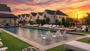 Una piscina con sillones de descanso y un atardecer de fondo.