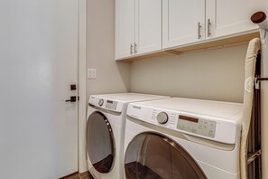 A laundry room with two front-loading washing machines and a cabinet above. - Magnolia Manor at College Station & Texas A&M (College Station)