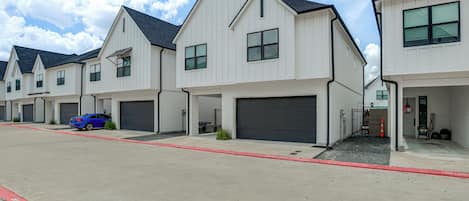 A row of modern two-story houses with attached garages, a red curb, and a blue car parked in front.