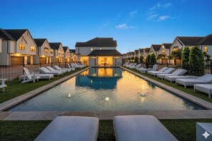 Blick auf einen Poolbereich eines Hotels mit mehreren Gebäuden, einem Schwimmbecken und Liegestühlen.