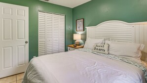 Un dormitorio con una cama, una mesita de noche, una lámpara, una puerta y una pared con un cuadro enmarcado.