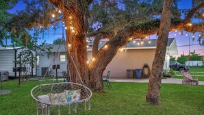 Un patio trasero con una silla colgante, una hamaca y luces de cadena.