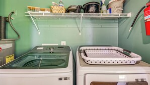Zona de lavandería con lavadora, secadora y estantes con productos de limpieza.