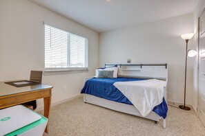 Een slaapkamer met een bed, een bureau, een laptop, een raam met jaloezieën en een vloerlamp.