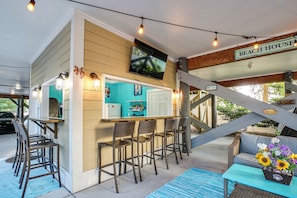 Ein Strandhaus mit Bar, Sitzgelegenheiten im Freien und einer Treppe.