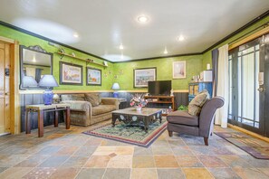 A living room with a sofa, armchair, coffee table, and a television. There are framed pictures on the wall and a mirror. - Lake Arrowhead Retreat w/ Game Loft & Media Room (Lake Arrowhead)