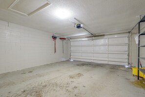 Un garage aux murs blancs et au sol en béton, doté d’une porte de garage fermée et d’un luminaire fixé au plafond.