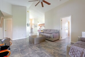 Ein großzügiger Wohnraum mit grauem Sofa, Couchtisch und Deckenventilator.