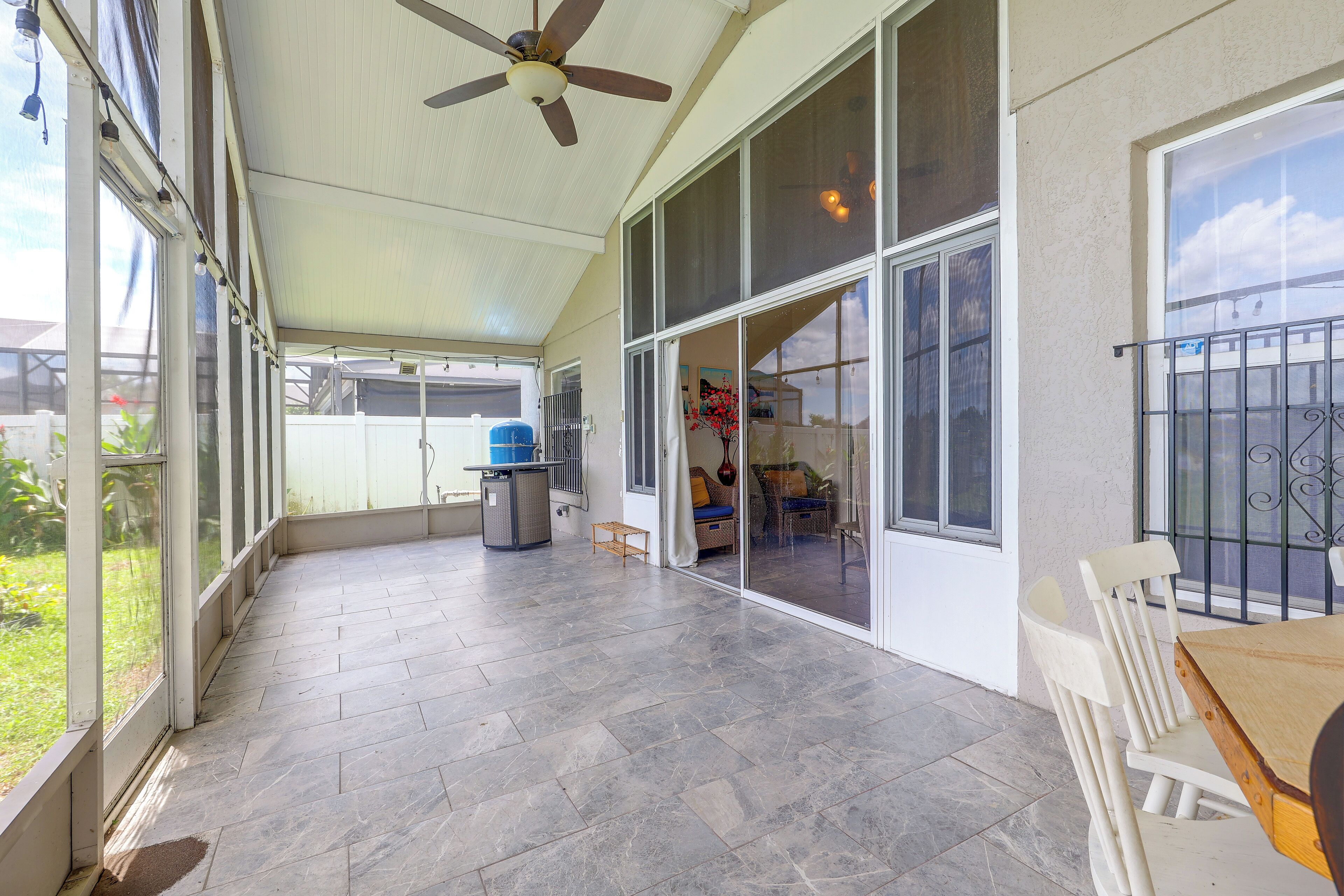 A covered patio area with a ceiling fan, large windows, and a tiled floor.