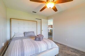 Ein Schlafzimmer mit einem Bett, einem Deckenventilator und Blick in die angrenzende Küche.