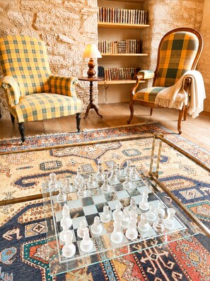 A room with a chessboard, two armchairs, a bookshelf, and a patterned rug.