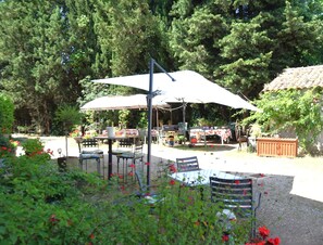 An outdoor patio area with tables and chairs under umbrellas, surrounded by greenery and trees. - La Tourelle - Peace and Charm in Cathar Country (Lauraguel)