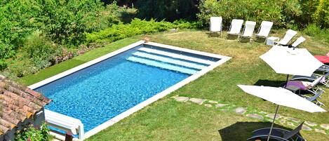 A rectangular swimming pool surrounded by a well-maintained lawn, with several lounge chairs and umbrellas arranged for relaxation.