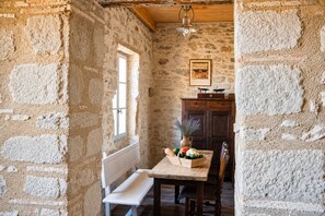 A rustic stone-walled room with a wooden bench, a table with fresh produce, and a wooden cabinet.