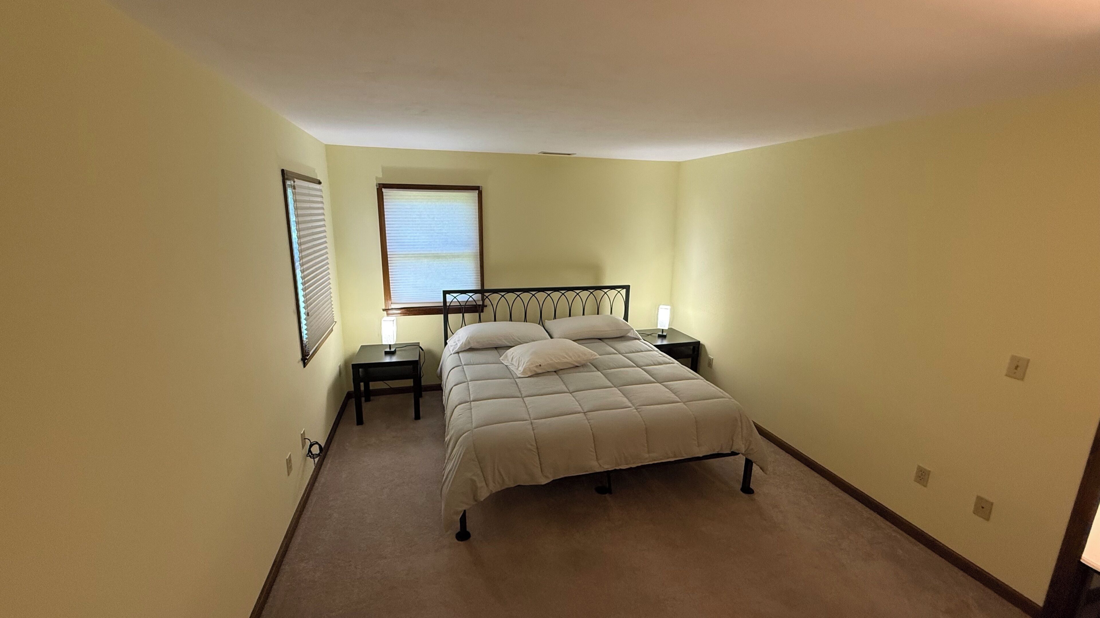 A bedroom with a bed, bedside tables, a lamp, and a window.