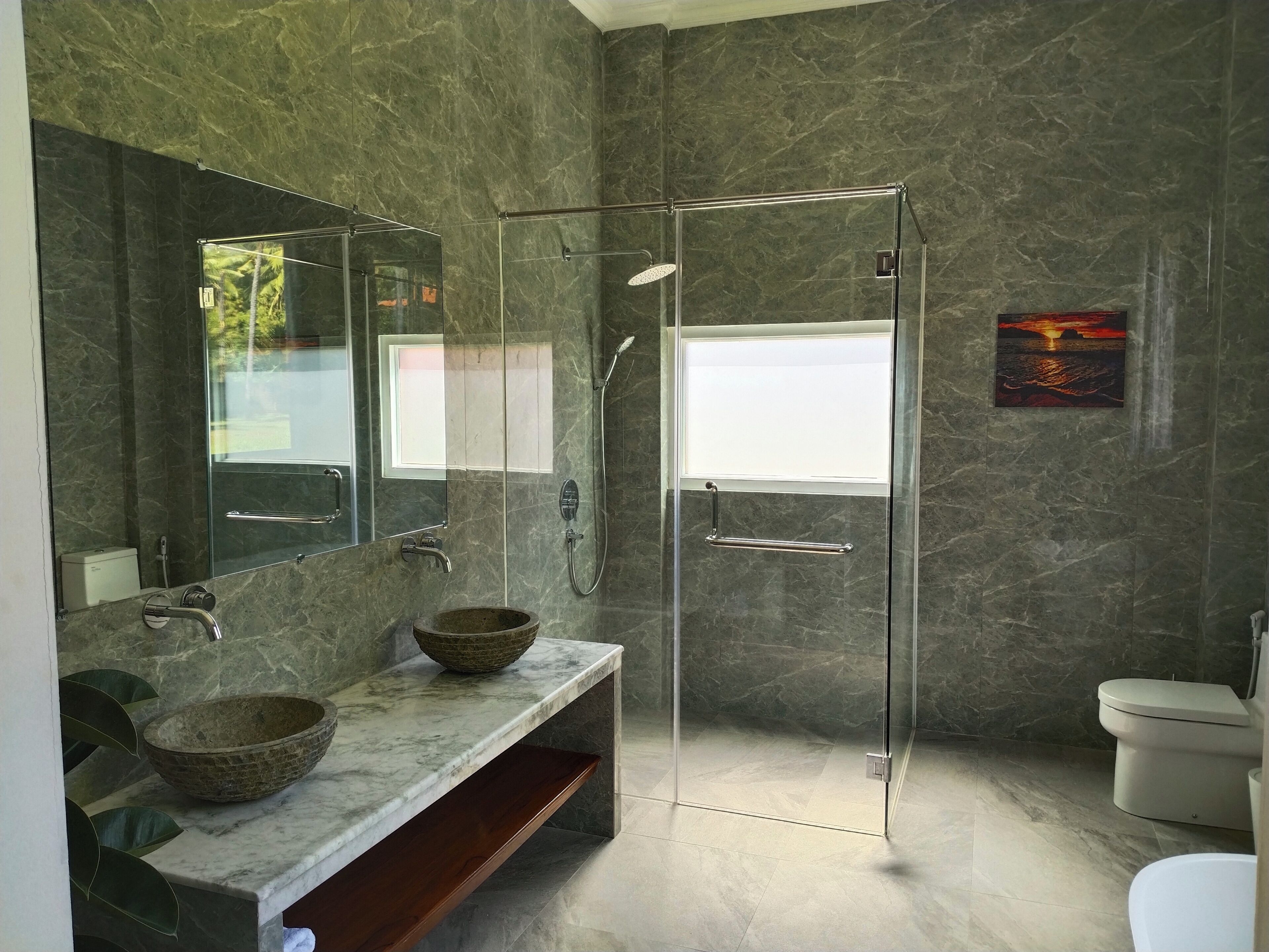 A modern bathroom with a glass-enclosed shower, a marble vanity, and a large mirror.