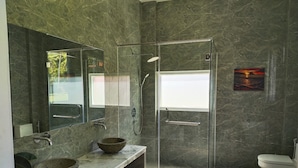 Un baño moderno con ducha de vidrio, tocador de mármol y un espejo grande.