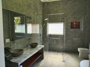 Un baño moderno con ducha de vidrio, tocador de mármol y un espejo grande.