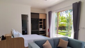 Una habitación de hotel moderna con cama, sofá, escritorio de madera y puerta corrediza de vidrio que da a un jardín.