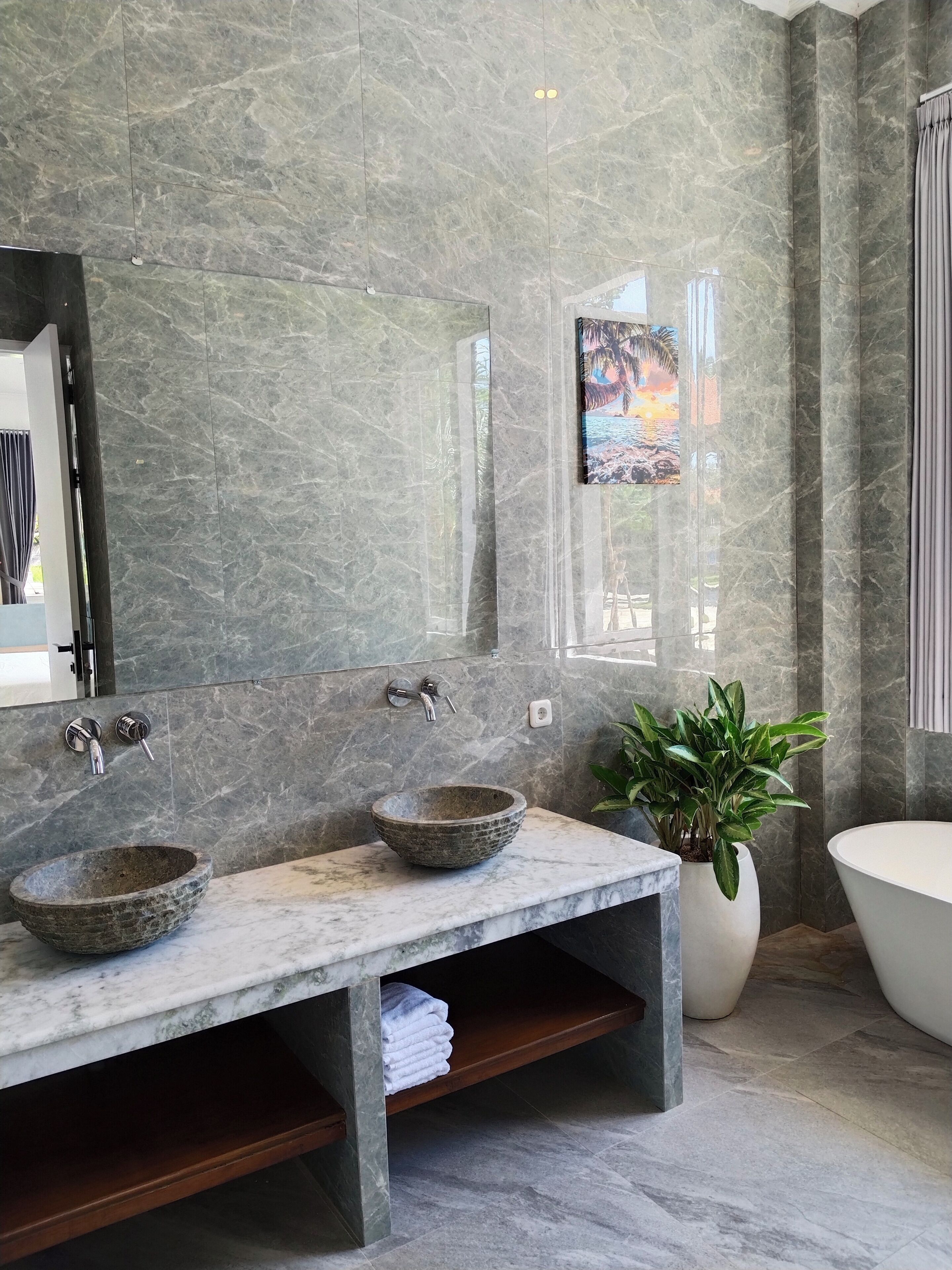 A bathroom with a marble vanity, two sinks, a large mirror, a bathtub, and a potted plant.