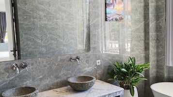 A bathroom with a marble vanity, two sinks, a large mirror, a bathtub, and a potted plant.