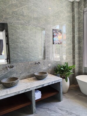 Un baño con tocador de mármol, dos lavamanos, un espejo grande, una bañera y una planta en maceta.