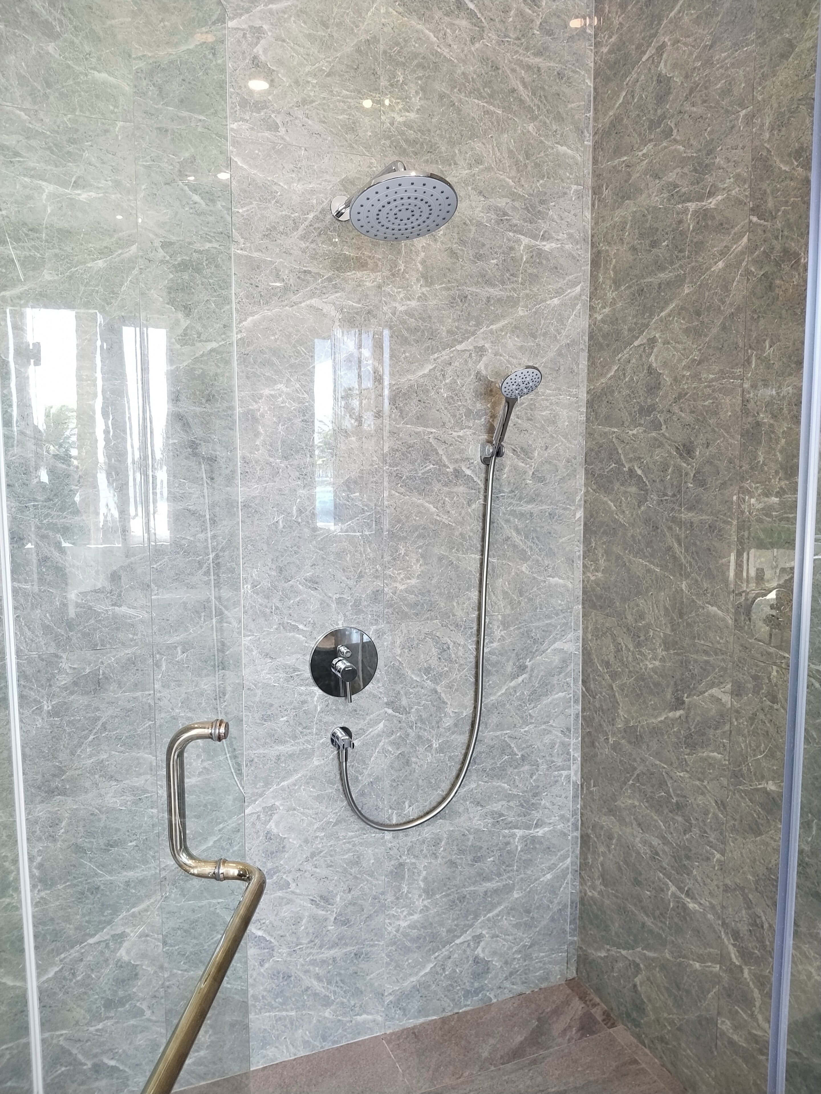 A shower with a handheld showerhead and a wall-mounted rain showerhead, both with chrome finishes, against a marble wall.