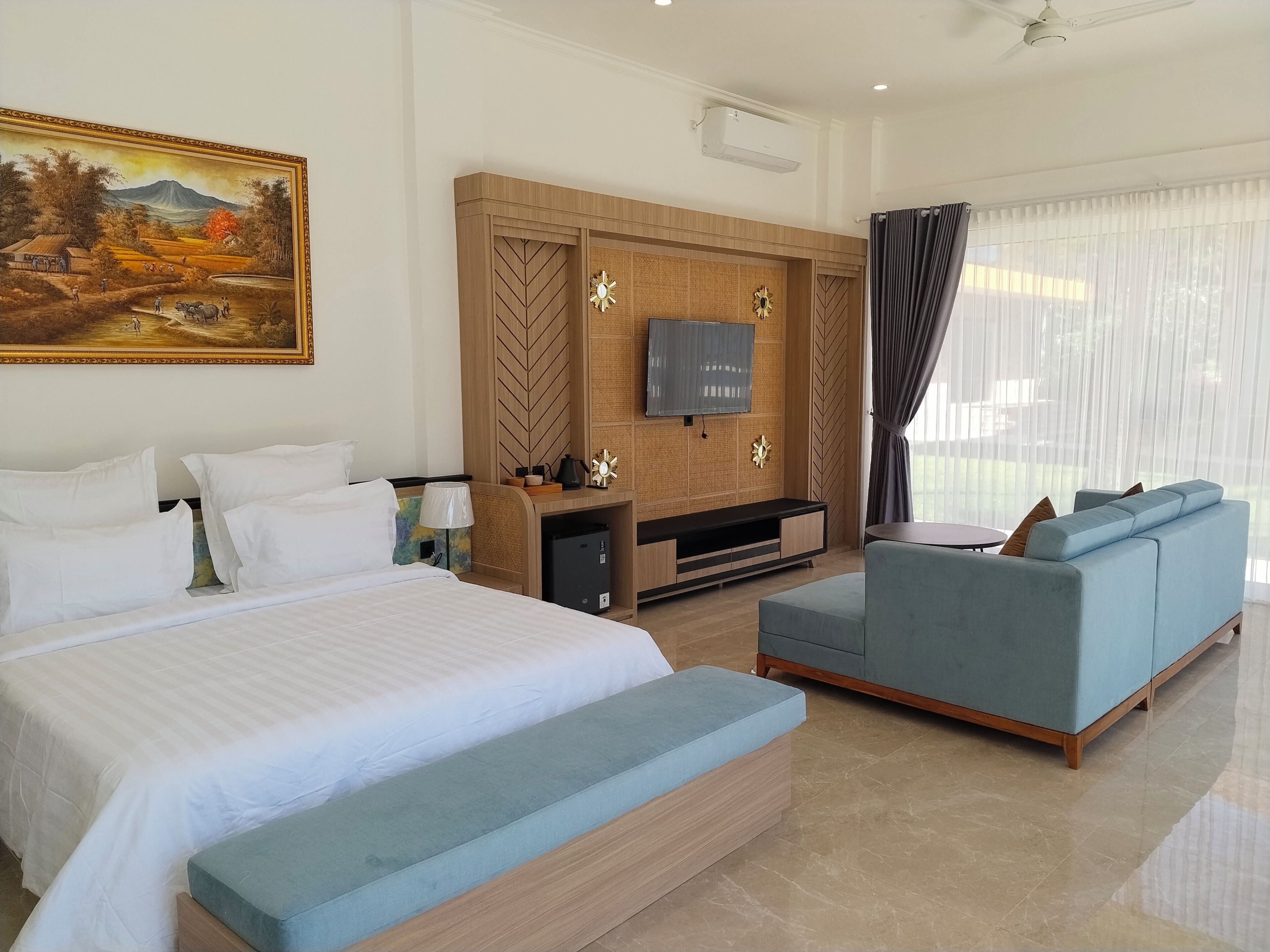 Quarto de hotel com cama, sofá, televisão e um quadro na parede.