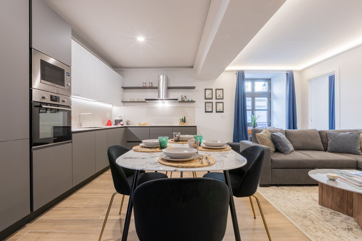 A modern kitchen with built-in appliances, a dining area with a round table and chairs, and a living room with a sofa and a coffee table.