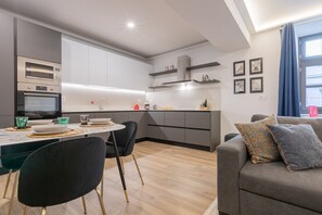 Une cuisine moderne dotée d’appareils électroménagers intégrés, un coin repas avec une table ronde et des chaises, et un espace de détente avec un canapé et des coussins.