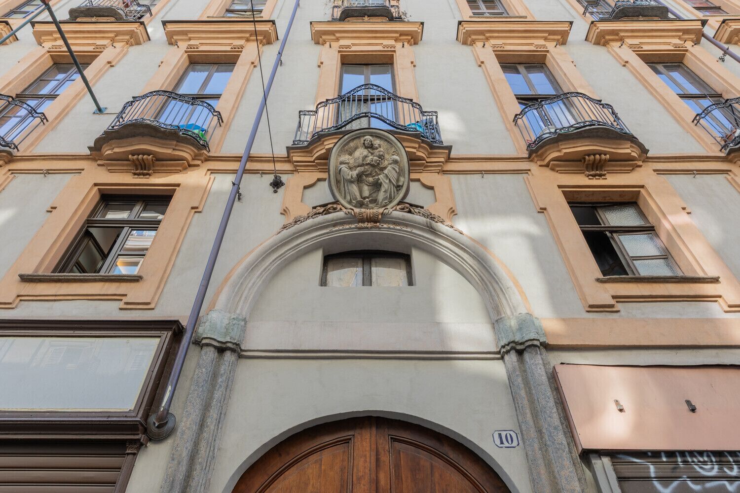 Une façade d’immeuble avec une entrée centrale en arc de cercle, de nombreuses fenêtres et des balcons dotés de garde-corps décoratifs.