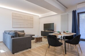 Un salon moderne comprenant un canapé, une table basse, une table à manger avec des chaises, un téléviseur à écran plat et une grande œuvre d’art abstraite accrochée au mur.