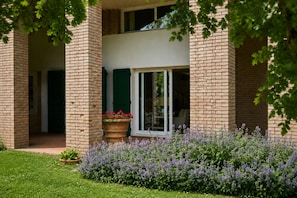 A two-story building with a brick facade, a glass door entrance, and a garden with purple flowers.