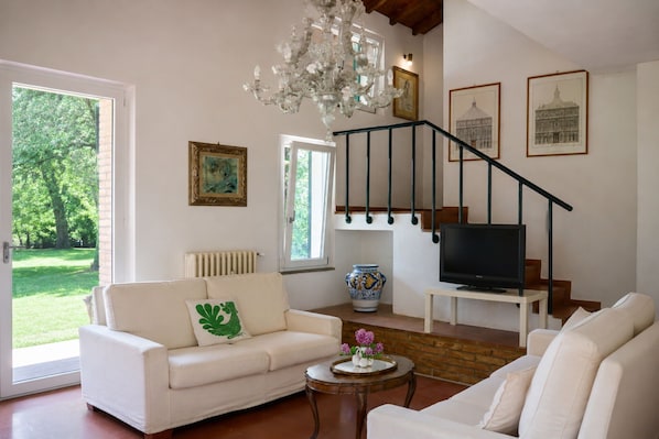 A living room with a white sofa, a coffee table, a TV, a chandelier, and a staircase.